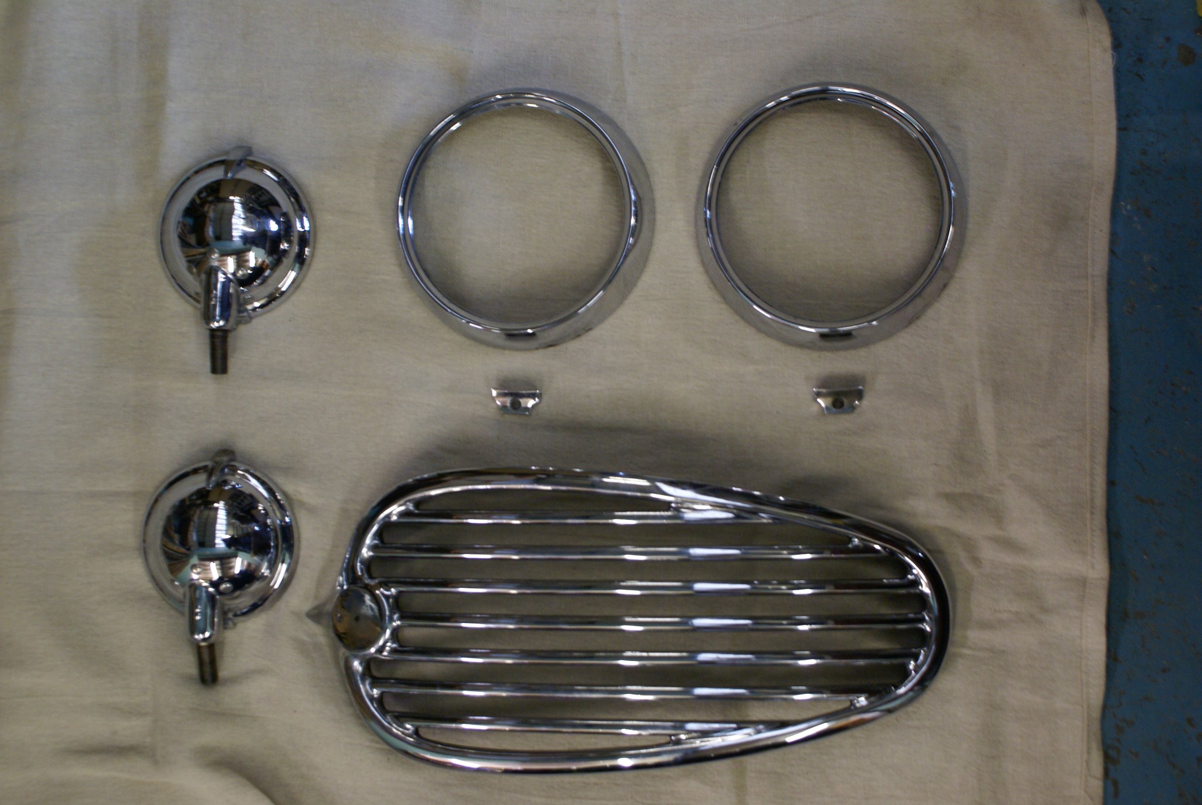 Re-chromed spot lamps, headlamp rims and a wing grille laid out on a cloth